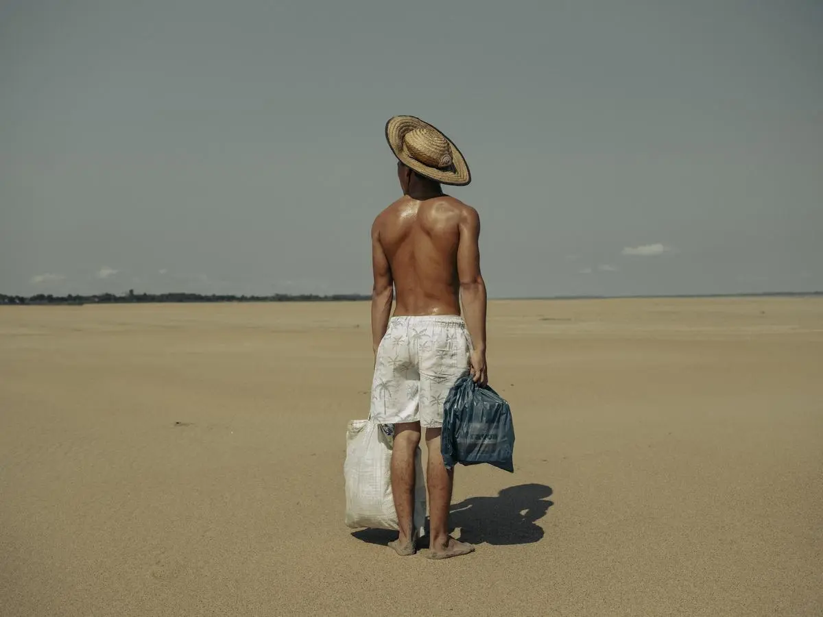 Der Titel des Bildes lautet „Droughts in the Amazon“. Der junge Mann ist mit Lebensmitteln auf dem Weg zu seiner Mutter. Er muss dabei zwei Kilometer durch ein ausgetrocknetes Flussbett in der Amazonasregion gehen.